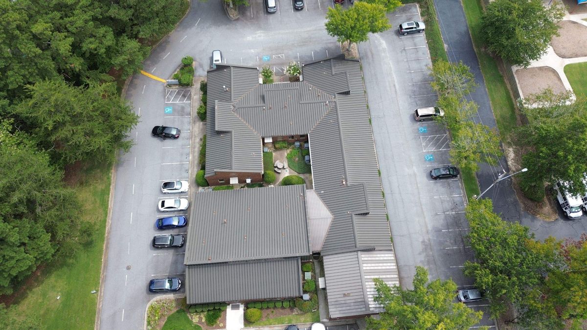 Aerial drone overview of commercial metal building before roof replacement — deteriorated panels visible